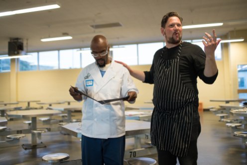 Derry "Brother D" Brown looks down at his completion certificate while chef Huw Thornton, right, talks to attendees of the graduation dinner of the Quentin Cooks program at San Quentin State Prison in San Quentin, Calif., on Wednesday, May 22, 2019. The all-volunteer program, brings chefs and inmates together to teach inmates how to work in a commercial kitchen. (Randy Vazquez/Bay Area News Group)